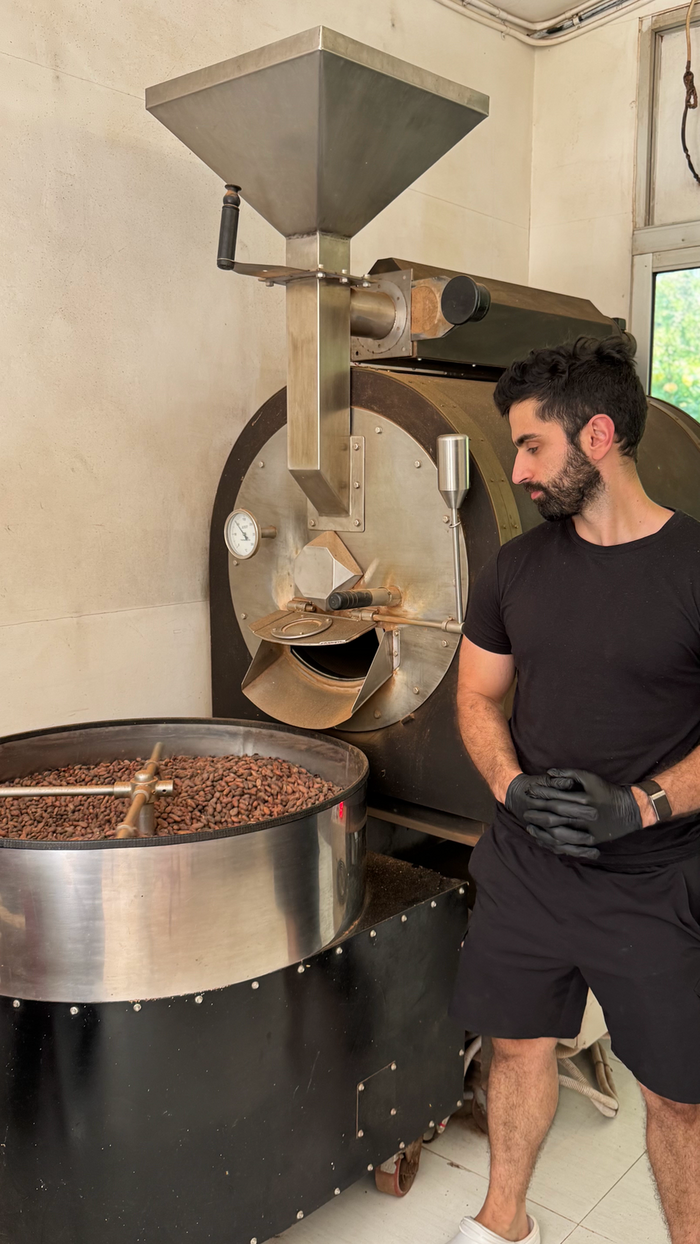Ali at the small-batch roaster beside a drum of cacao beans in the Bali facility